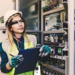 Young_woman_industrial_service_engineer_wearing_white_worker_headwear_standing,_working,_checking_conducts_a_safety_check_front_of_a_control_panel_read_and_writing_notes_about_technical_problems_in_boiler_energy_control_room_of_modern_thermal_or_nuclear_p