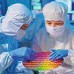 two_asian_technicians_in_sterile_coverall_hold_wafer_with_gloves_that_reflects_many_different_colors_and_check_it_at_semiconductor_manufacturing_plant